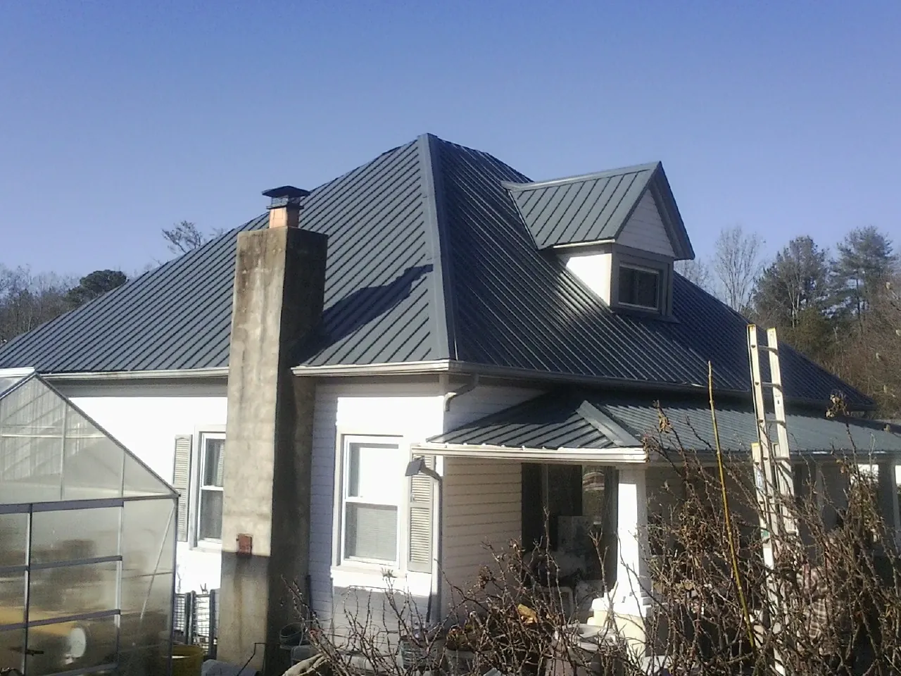 Dark blue standing seam metal roof on a white farmhouse with dormer — Slate & Tile Roof Repair by Roofing Brothers in Colfax