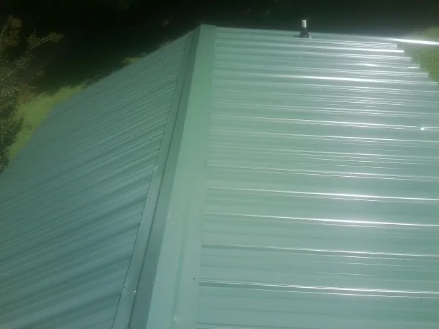 New green metal panels meeting at the ridge of a roof — Flat Roof Repair work by our crew in Colfax