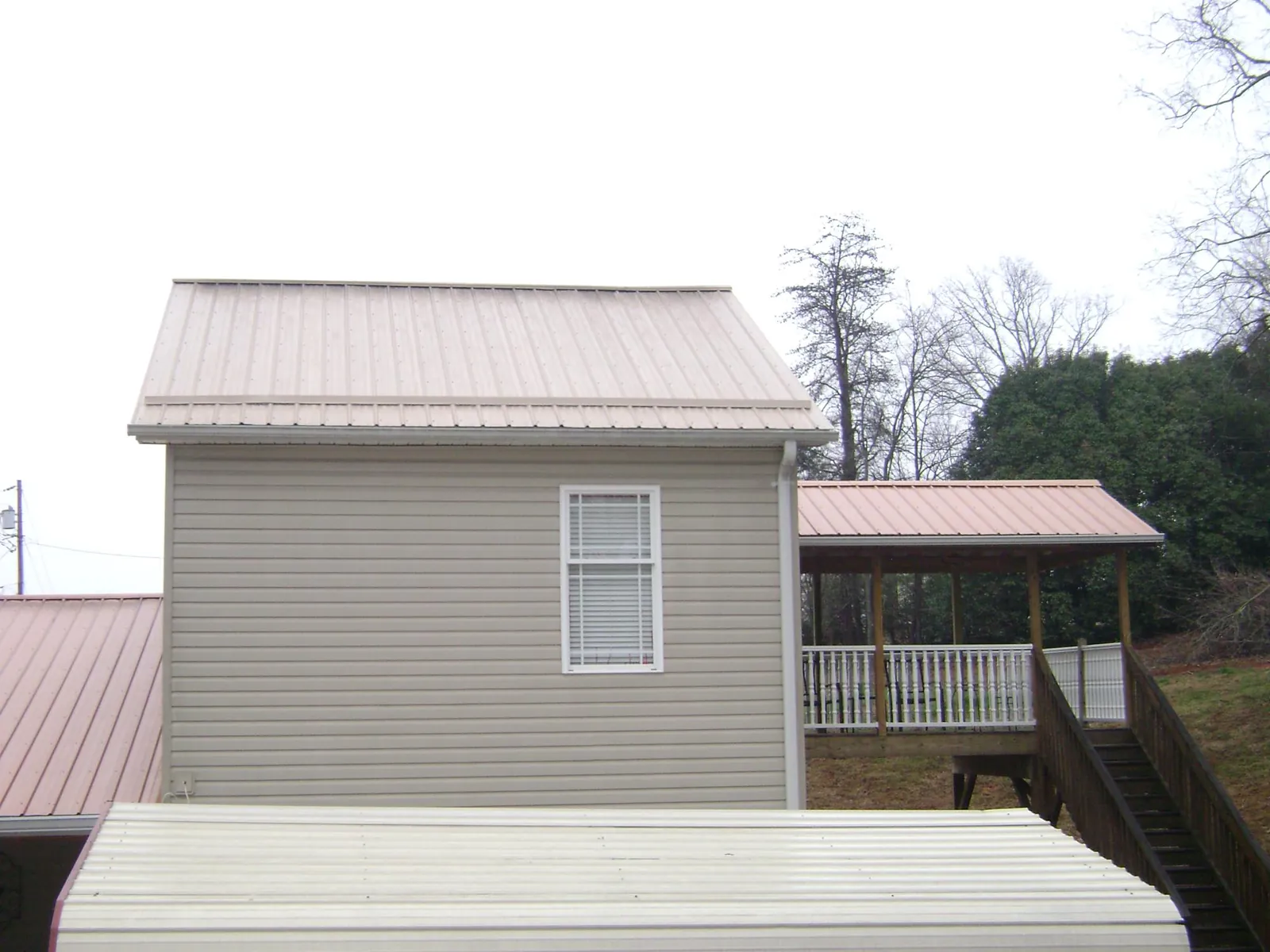 Tan metal roofs on a two story addition and attached porch, from a Roof Replacement job in Colfax